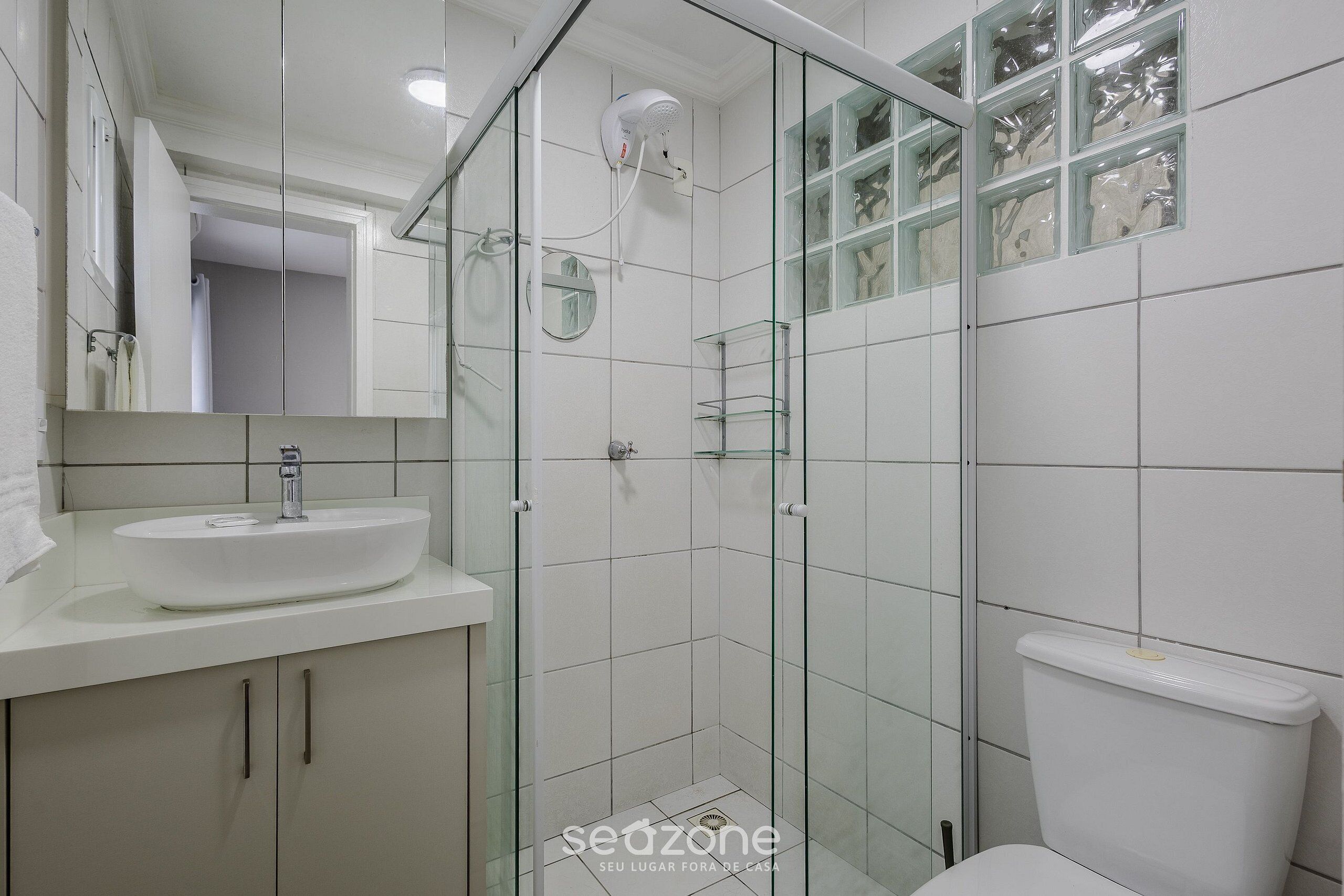 Un baño moderno con ducha de vidrio, lavamanos blanco y un inodoro.