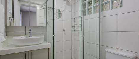 Un baño moderno con ducha de vidrio, lavamanos blanco y un inodoro.