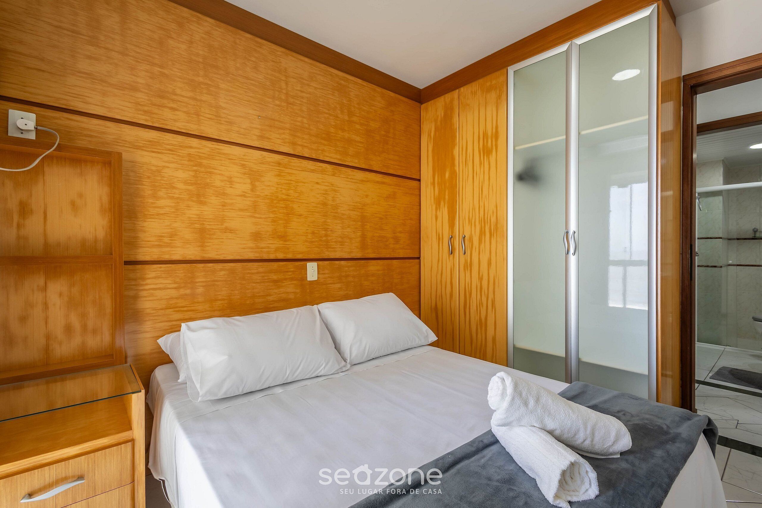 Ein Hotelzimmer mit einem hölzernen Kopfteil, einem Bett mit weißer Bettw äsche, einem Schrank mit Glastüren und einem Handtuch auf dem Bett.
