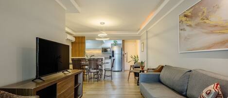 A modern living room with a flat-screen TV, a sofa, and a dining area with chairs and a table.