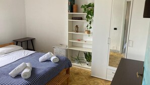Een slaapkamer met een bed, een klein tafeltje, een kledingkast en een bloempot met plant.
