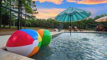 Una piscina con pelotas de playa, un paraguas verde y sillas de descanso.