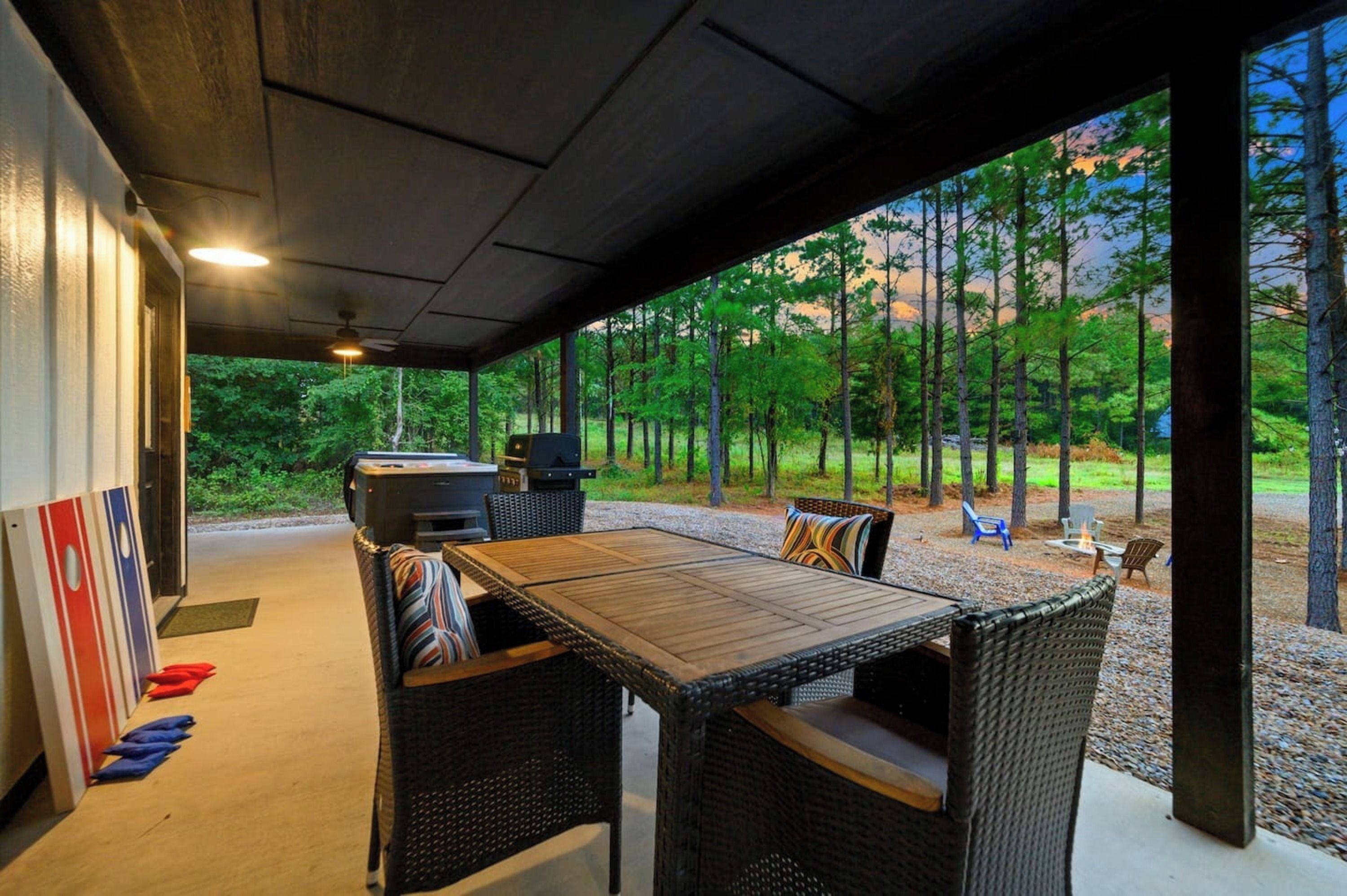 Un patio al aire libre con una mesa de madera y sillas de mimbre, una parrilla y vistas a un bosque.