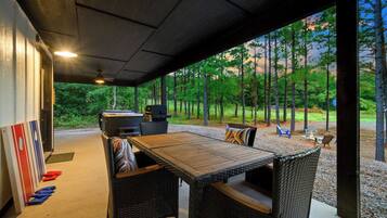 Un patio al aire libre con una mesa de madera y sillas de mimbre, una parrilla y vistas a un bosque.