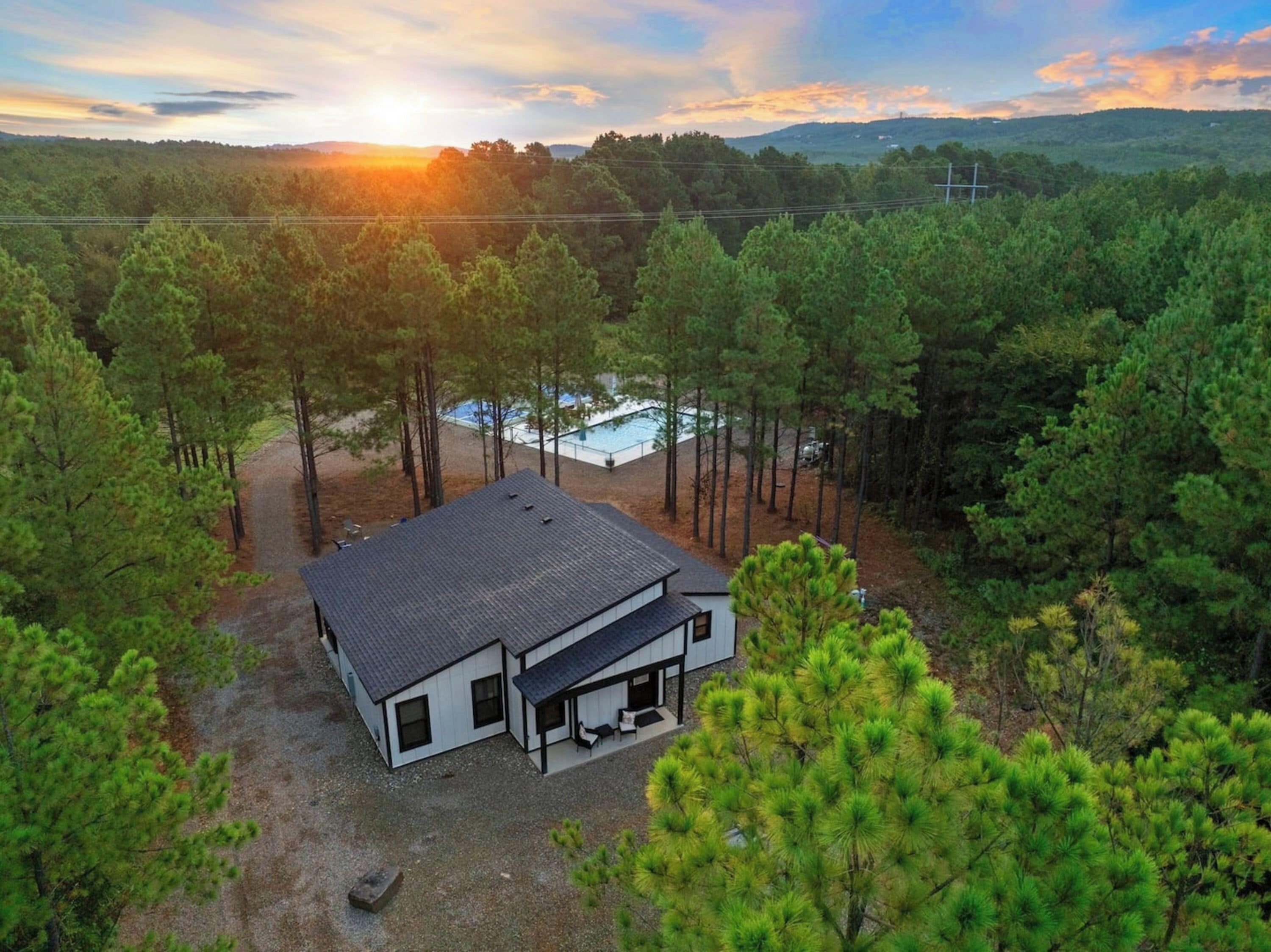 A modern two-story house with a large deck and a swimming pool, surrounded by dense pine trees.