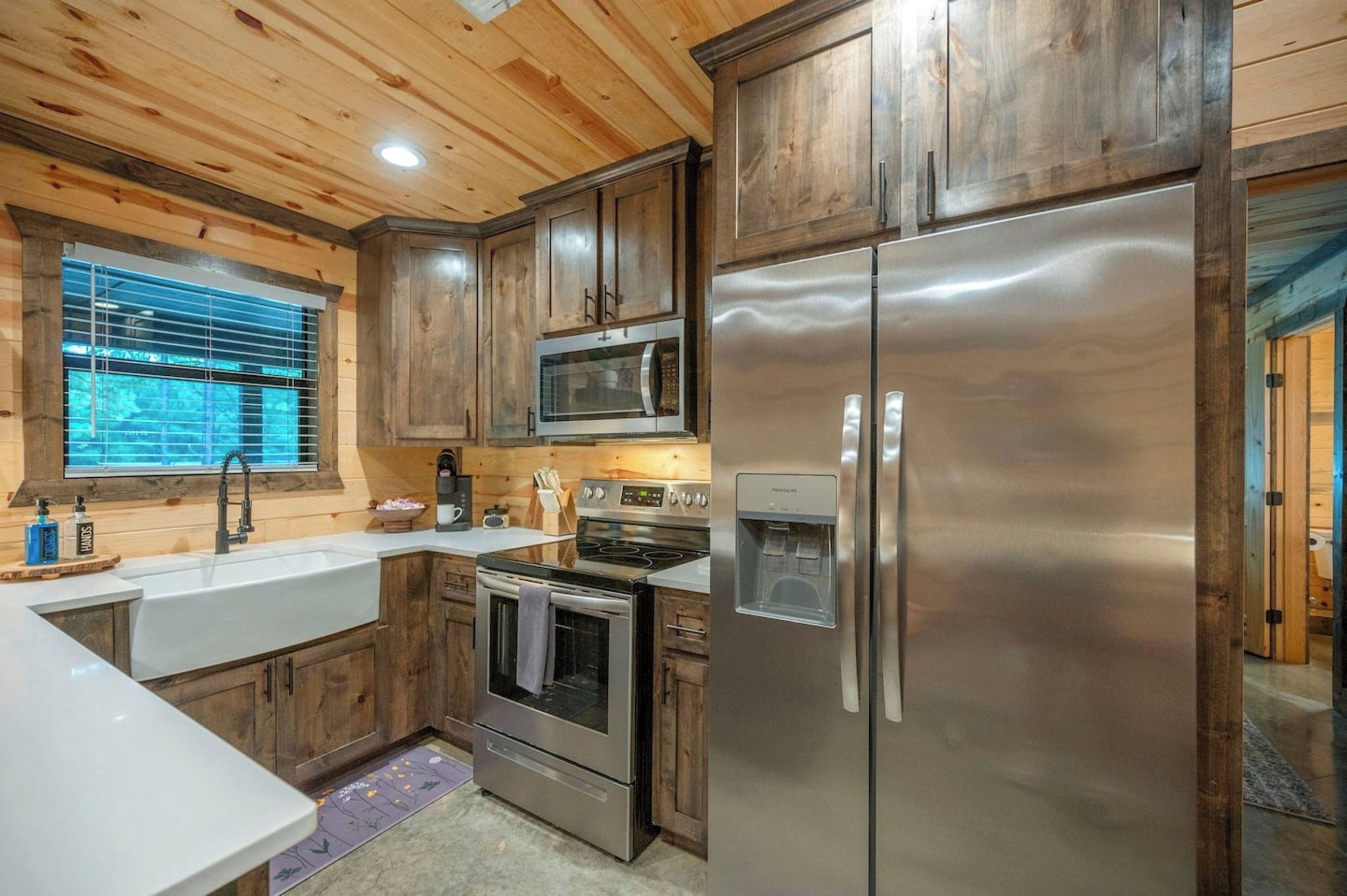 A modern kitchen with wooden cabinets, stainless steel appliances, and a window with blinds.