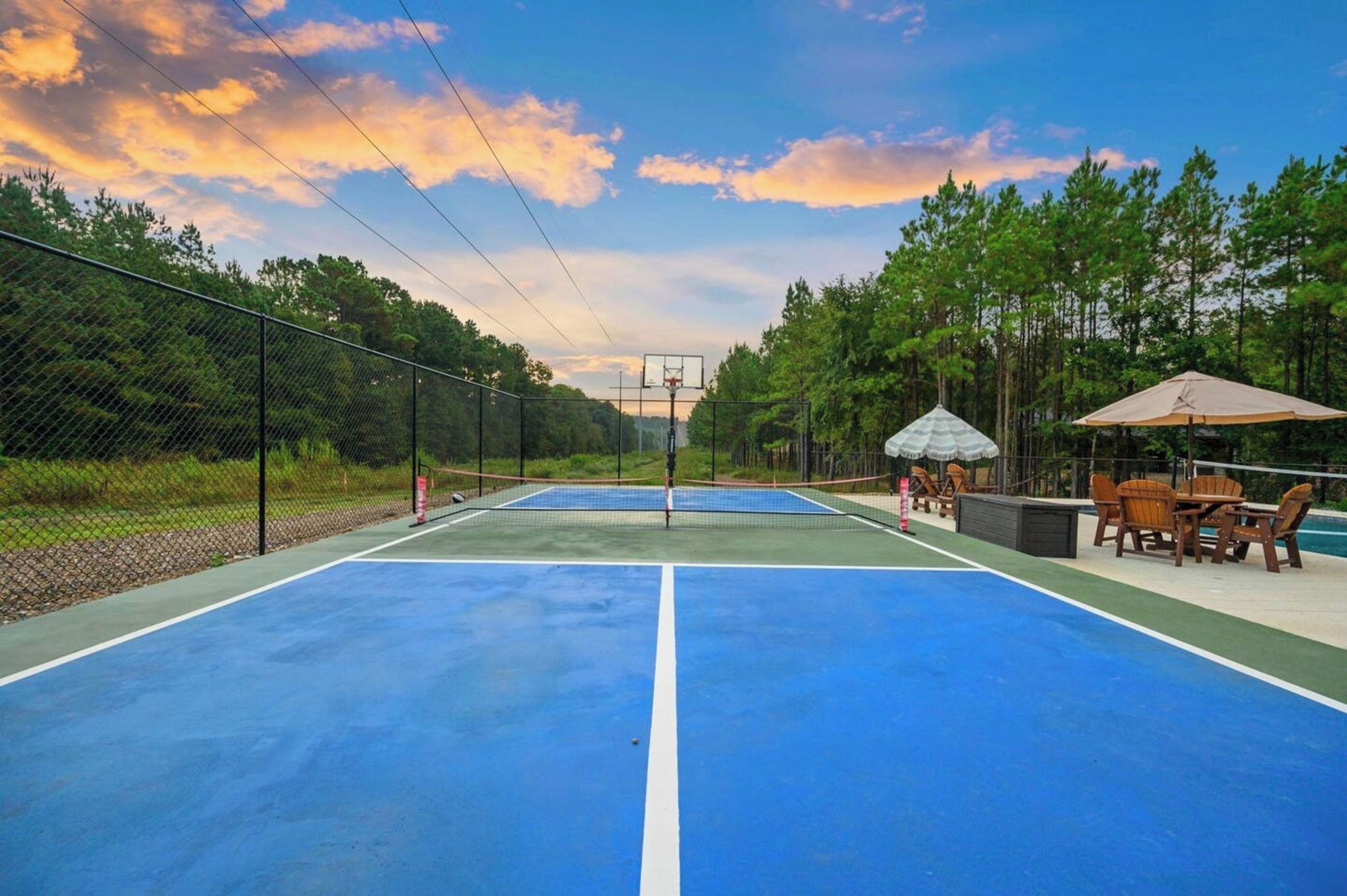Un terrain de basket en plein air, équipé d’un panier et entouré d’une clôture, avec un espace aménagé comprenant des tables et des chaises.