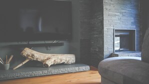 A modern living room with a stone fireplace, a mounted flat-screen TV, and a wooden log decoration.