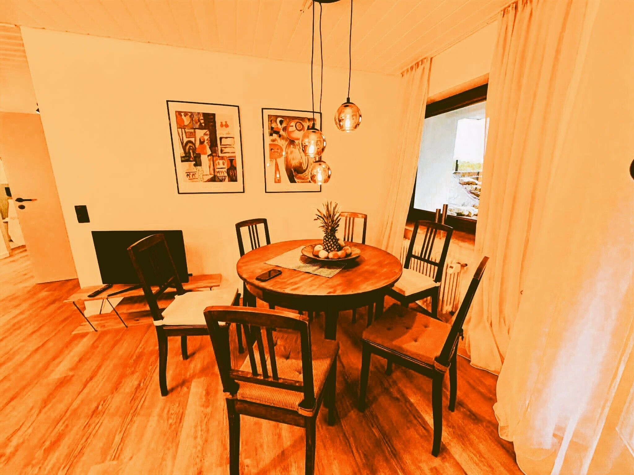 A dining area with a round table, chairs, a pineapple, and two framed artworks on the wall.