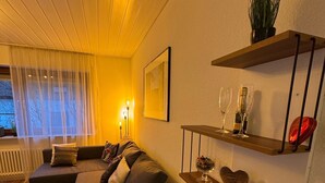 Un salon moderne avec un canapé d’angle, une petite table et des étagères murales ornées d’objets décoratifs.