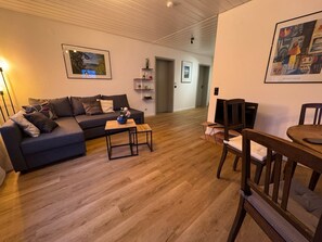 Sala de estar com sofá, mesa de centro, televisão e área de refeições.