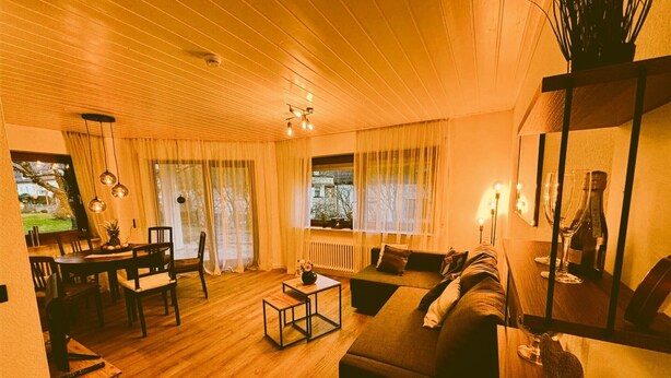 Un salon chaleureux avec un plafond en bois, un canapé, une table basse et un coin repas comprenant des chaises et une table.