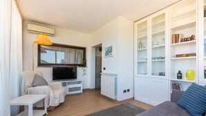 A modern living room with a flat-screen TV, a sofa, a small table, and a cabinet with glass doors. - Rental in Rome San Pancrazio Penthouse (Rome)