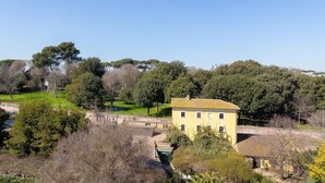 A yellow building with a tiled roof, surrounded by trees and greenery. - Rental in Rome San Pancrazio Penthouse (Rome)