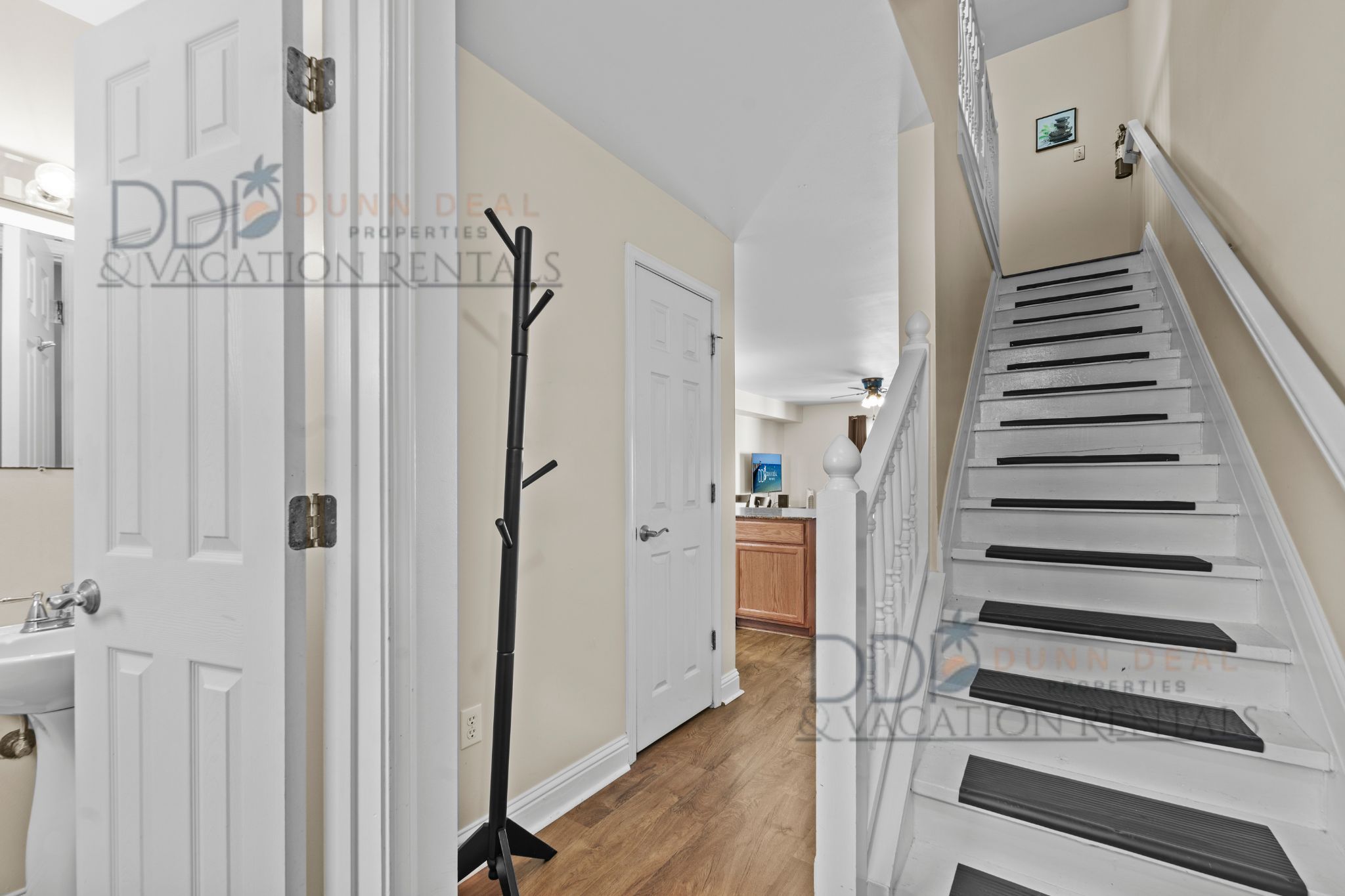 A hallway with a white door, a coat rack, and a staircase with white steps and black risers.