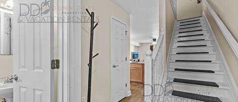 A hallway with a white door, a coat rack, and a staircase with white steps and black risers.