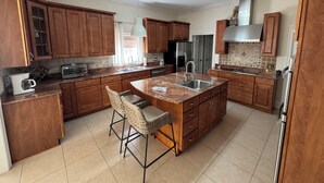 A modern kitchen with wooden cabinets, a stainless steel refrigerator, a built-in oven, and a large island with bar stools. - Beautiful Waterfront House with Pool sleeps 11 (Pass Christian)
