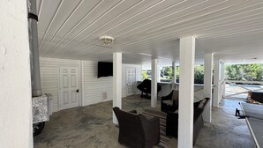 A covered outdoor area with white walls, a concrete floor, and wicker furniture. - Beautiful Waterfront House with Pool sleeps 11 (Pass Christian)