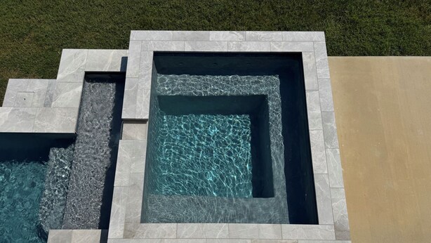 A modern outdoor swimming pool with a geometric design, surrounded by a stone border and a wooden deck. - Beautiful Waterfront House with Pool sleeps 11 (Pass Christian)