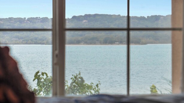 A view through a window with a blurred foreground, a body of water, and a forested hill in the background. - Lake Harbour on TRL For 6 (Hollister)