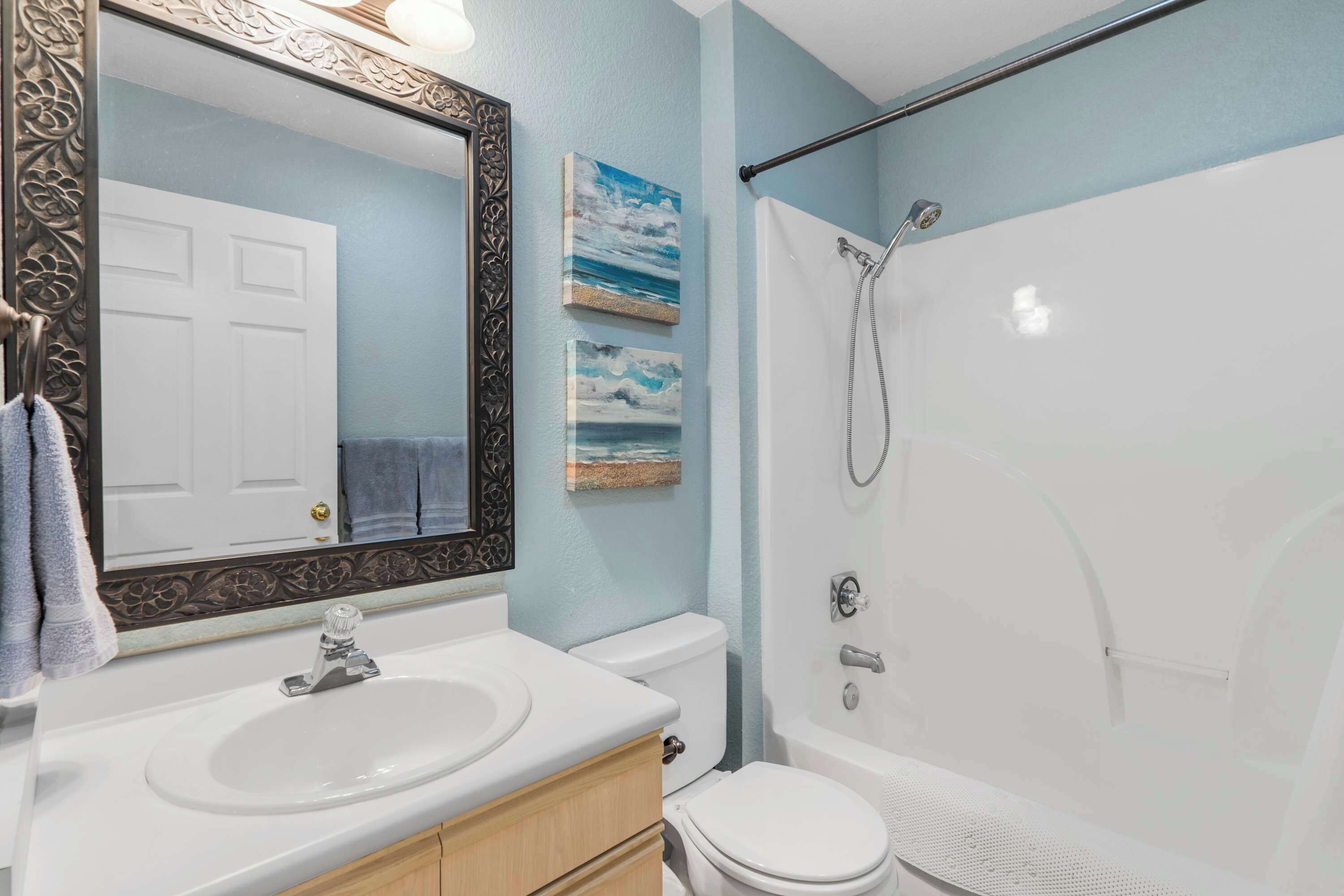 A bathroom with a white sink, a toilet, and a shower. There are two framed pictures on the wall.