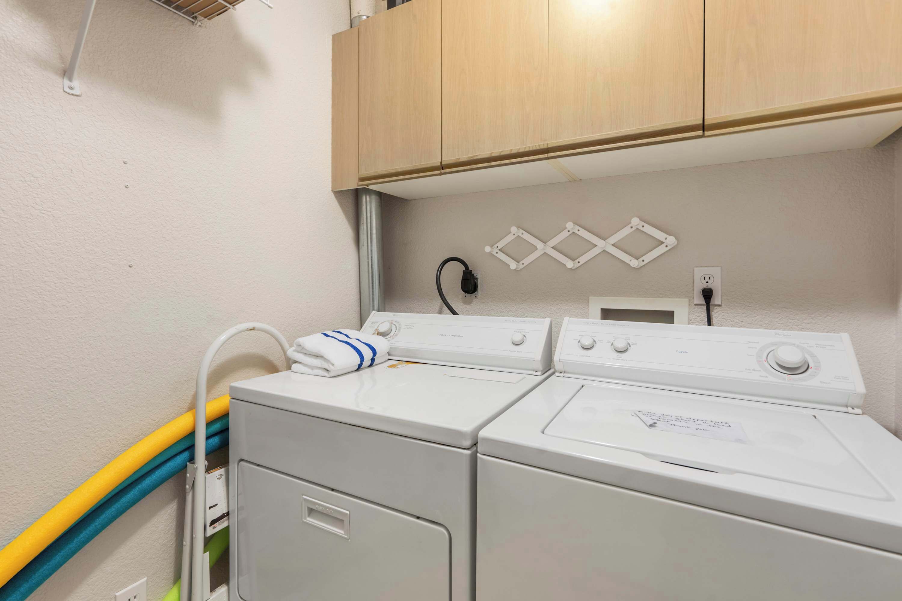 A laundry area with two front-loading washing machines, a dryer, and a wooden cabinet above.
