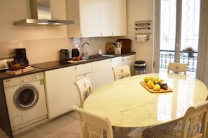 A compact kitchen with a washing machine, a dining table with chairs, and a balcony with a railing. - Bright apartment near Jardin du Luxembourg (Paris)