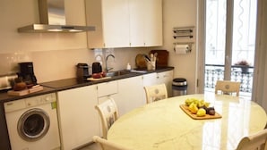 A compact kitchen with a washing machine, a coffee maker, and a dining table with chairs.