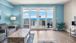 A spacious living room with a large sliding glass door leading to a balcony with a city view. - Beachfront condo w/ daily attraction tickets (Panama City Beach)