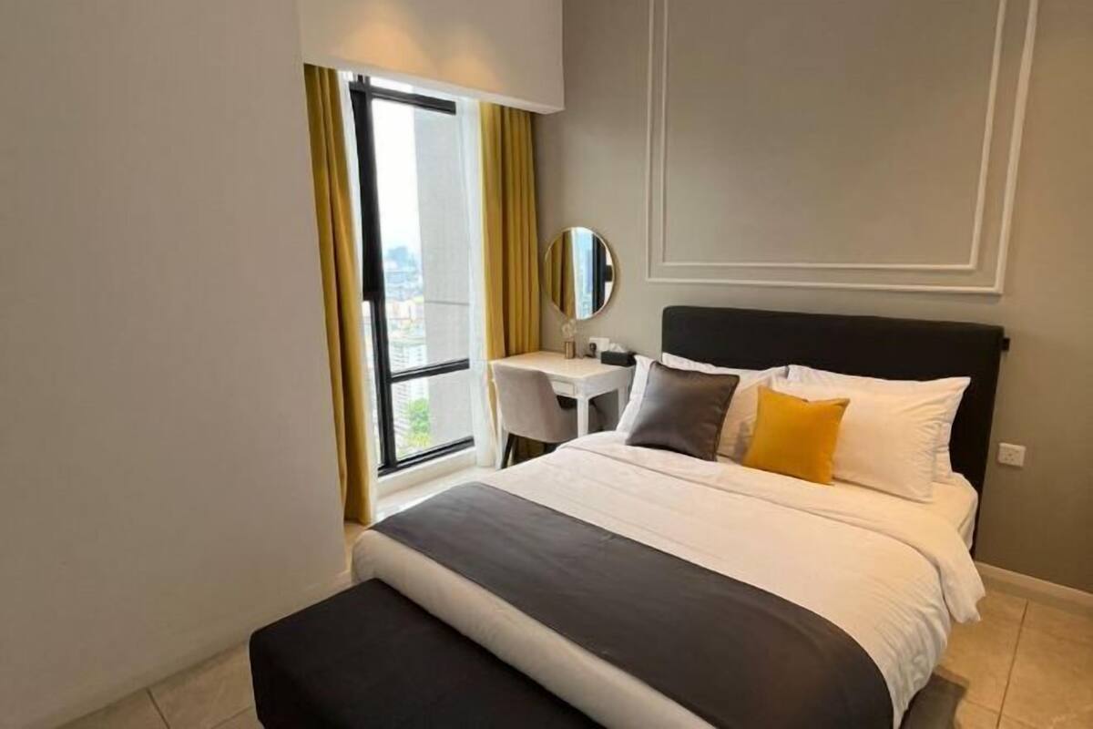 A hotel room with a bed, a desk, a chair, a window with curtains, and a view of the city.