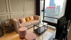 A modern living room with a beige sofa, two pink ottomans, a glass coffee table, and a large window with a city view. - AXON Bukit Bintang Luxury Condo 3BED 2BATH (HIGH FLOOR) (Kuala Lumpur)
