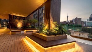 A rooftop terrace with wooden flooring, planters with greenery, and a cityscape view in the background. - AXON Bukit Bintang Luxury Condo 3BED 2BATH (HIGH FLOOR) (Kuala Lumpur)
