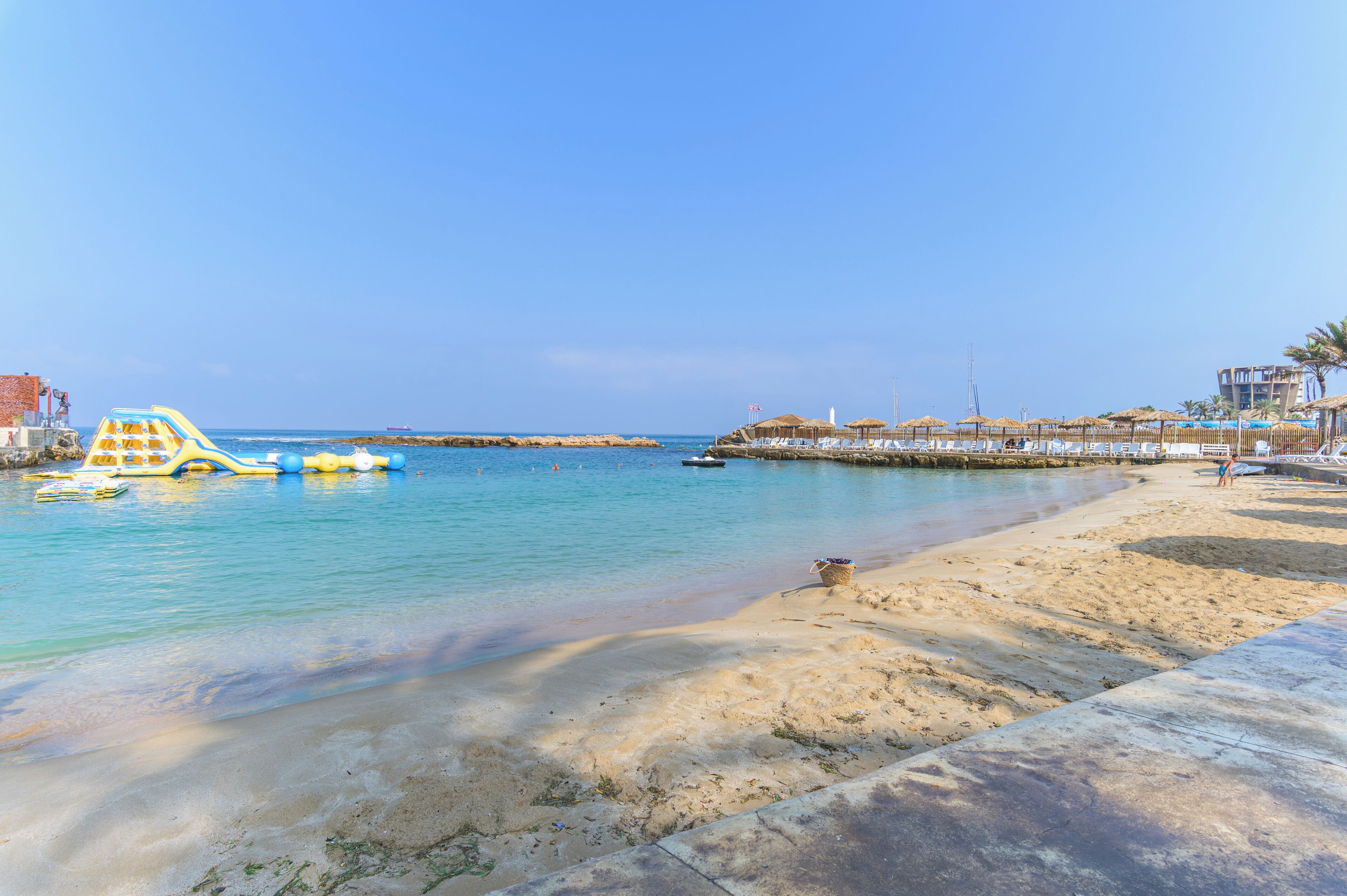 A beach with clear water, a sandy shore, and a pier with umbrellas.