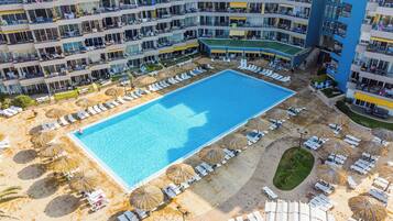 An aerial view of a hotel with multiple balconies, a central swimming pool, and sun loungers arranged around the pool.