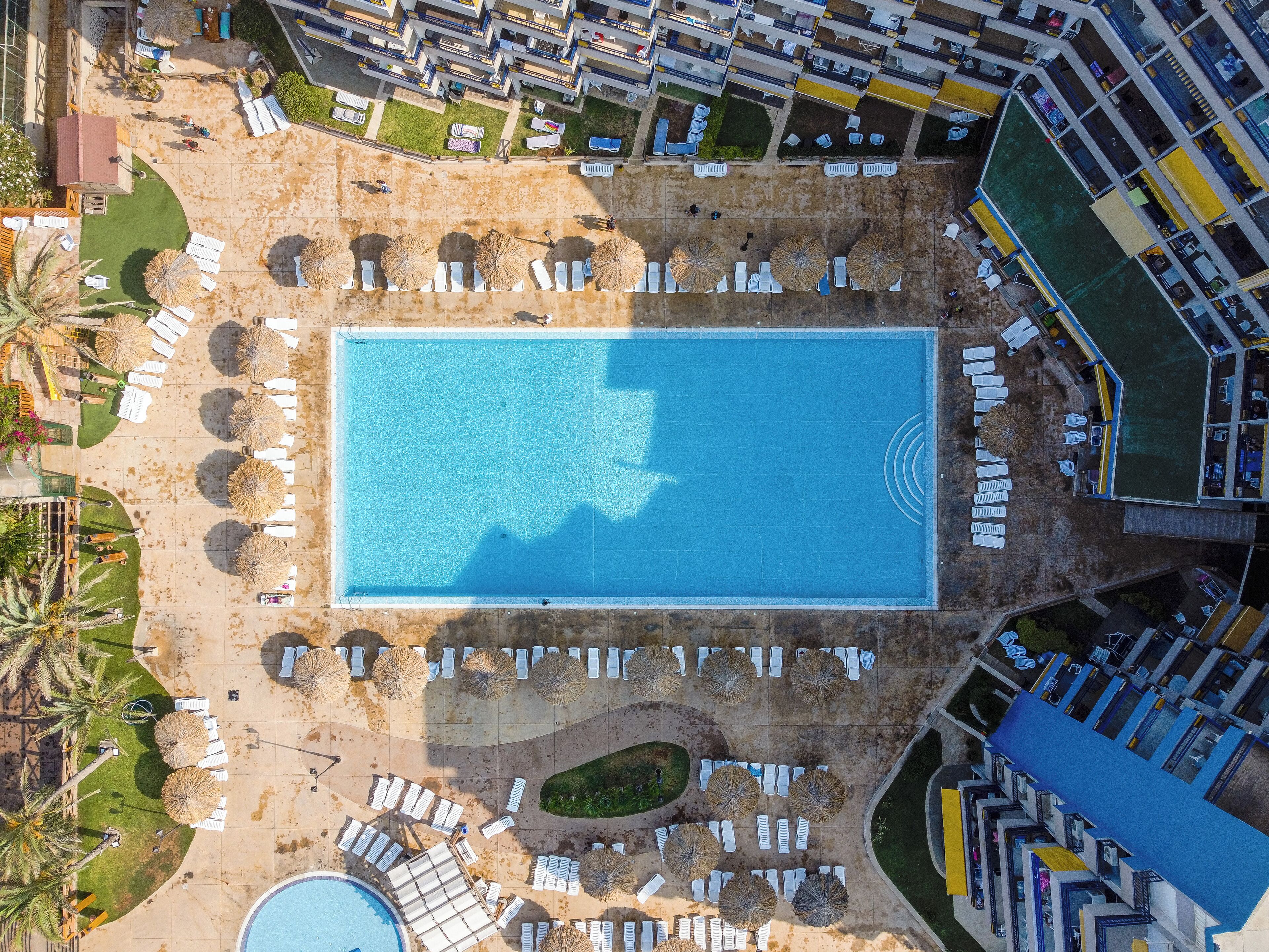 Vista aérea de um resort com uma piscina central, espreguiçadeiras e um complexo de edifícios.