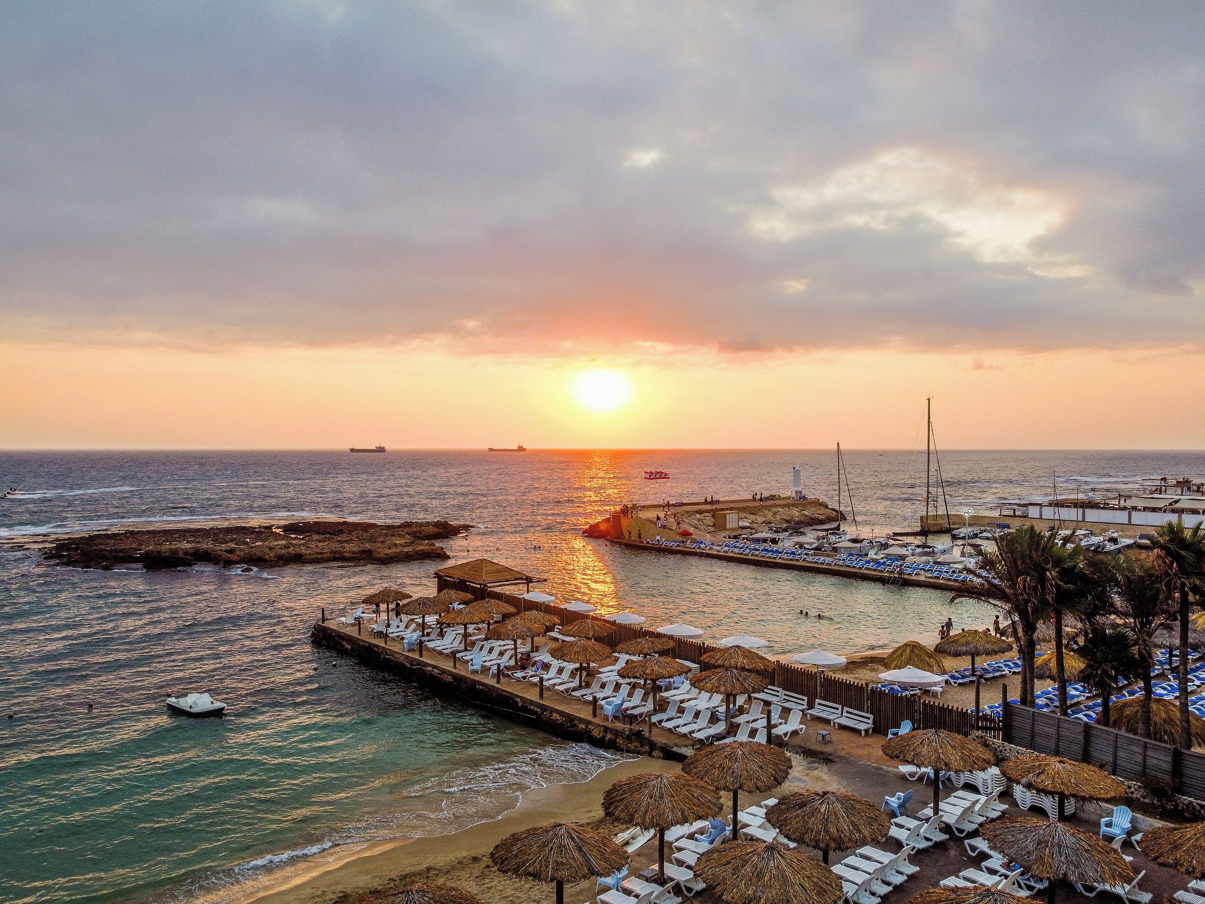 A coastal resort with a pier, beach umbrellas, and lounge chairs.