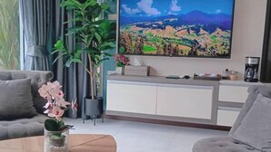 Olohuone, jossa on sohva, sohvapöytä, televisio ja ruukkukasvi.