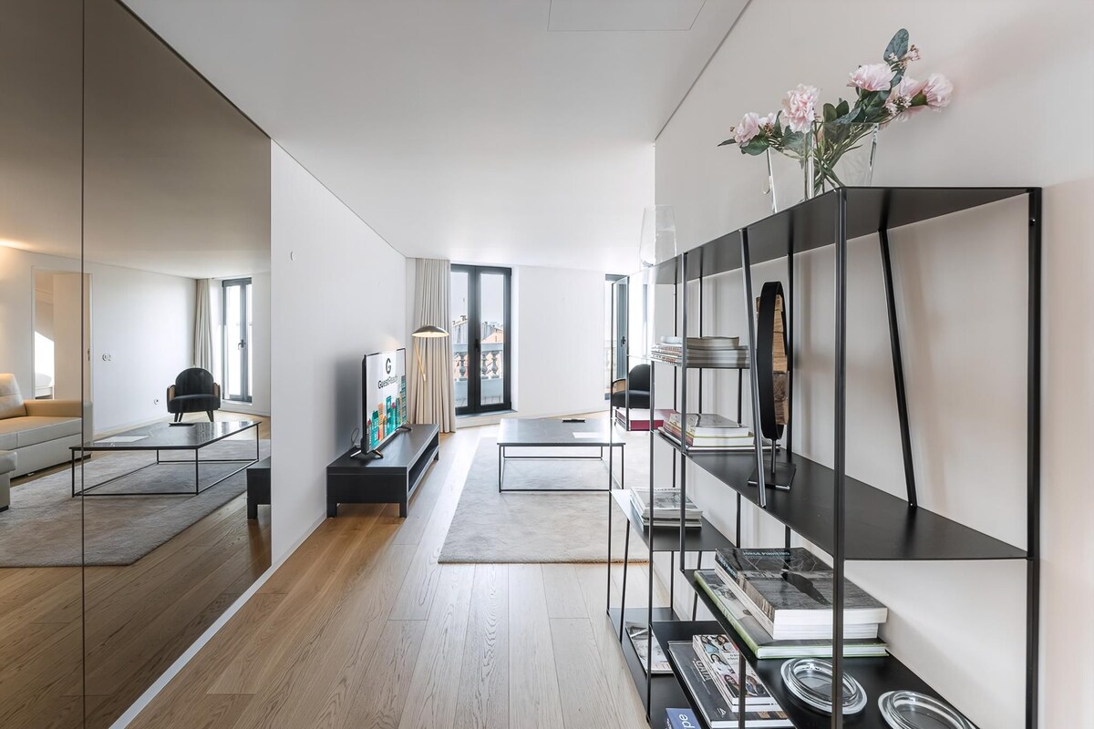Een moderne woonkamer met een bank, salontafel en een boekenkast vol boeken en decoratieve objecten.