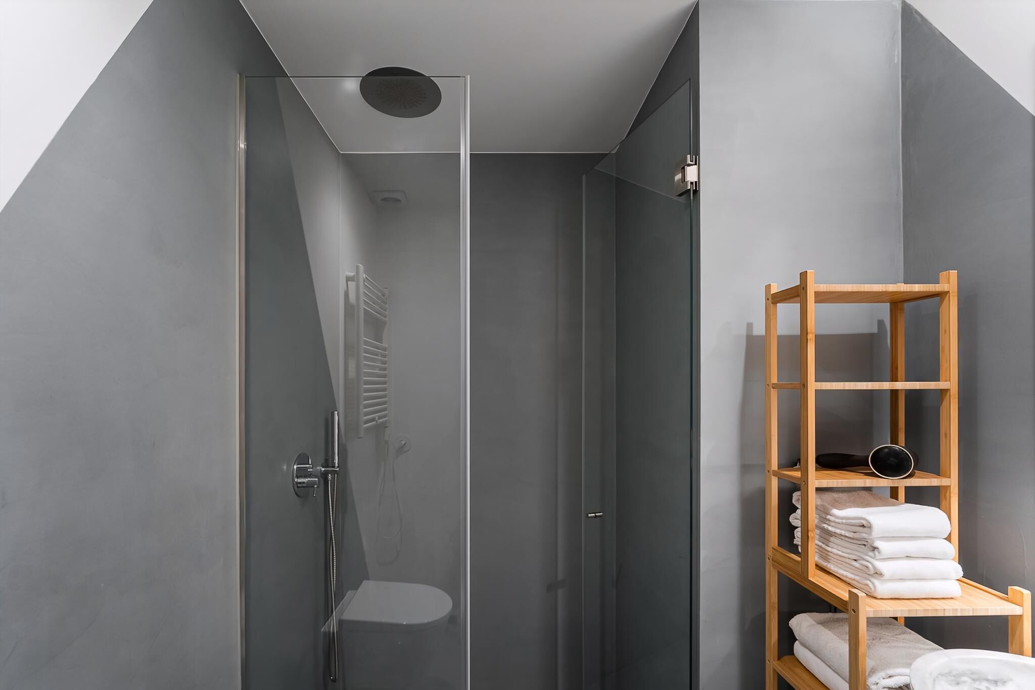 A modern bathroom with a glass-enclosed shower, a wooden shelf with towels, and a minimalist design.