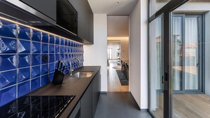 A modern kitchen with blue tiles, a black countertop, and a view to a balcony. - Guestready - Casas de Mompilher (Porto)