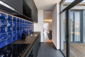 A modern kitchen with blue tiles, a black countertop, and a view to a balcony. - Guestready - Casas de Mompilher (Porto)