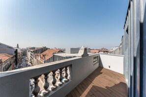 Een terras op het dak met een houten dek, een stenen balustrade en uitzicht op de stadsgezicht.