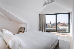 Een moderne hotelkamer met een groot bed, stadszicht door middel van raamwanden en een schuin dak.