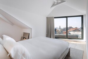 Een moderne hotelkamer met een groot bed, stadszicht door middel van raamwanden en een schuin dak.