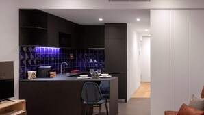A modern kitchen with dark cabinetry, a central island, and a seating area with a chair and sofa. - Guestready - Casas de Mompilher (Porto)