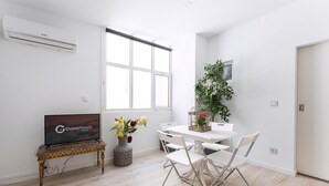A modern, well-lit room with a dining table, chairs, a TV on a stand, a potted plant, and a large window. - Guestready - Gold Leaf (Porto)