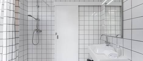 A modern bathroom with white tiled walls, a shower with a handheld showerhead, a sink with a mirror, and a towel on the sink.