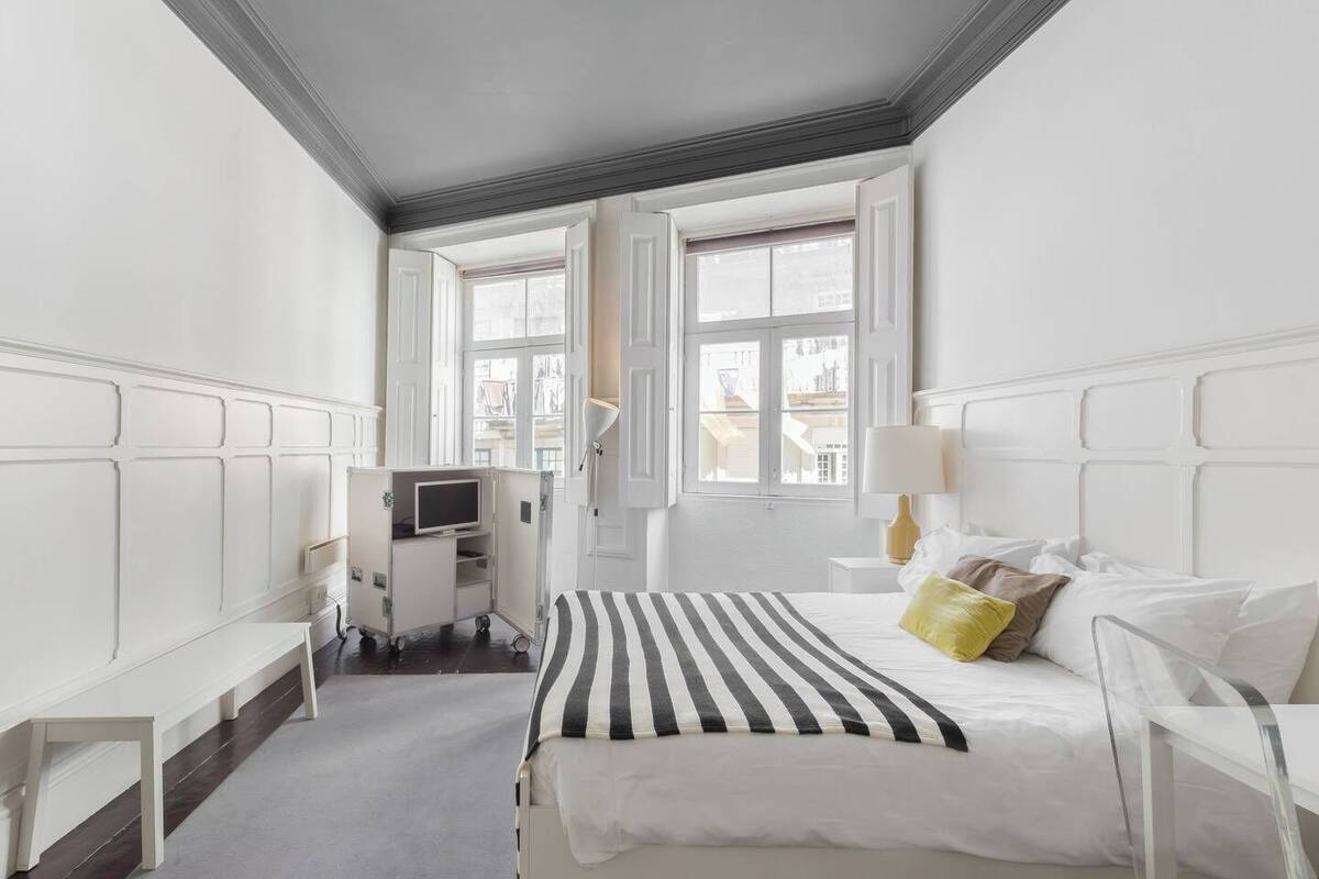 Une chambre d’hôtel avec un lit, des tables de chevet, une télévision et une fenêtre donnant sur des immeubles.