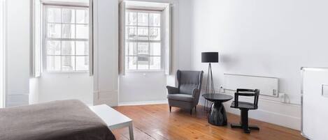 Una habitación con una cama, una silla, una mesita y una lámpara de pie.
