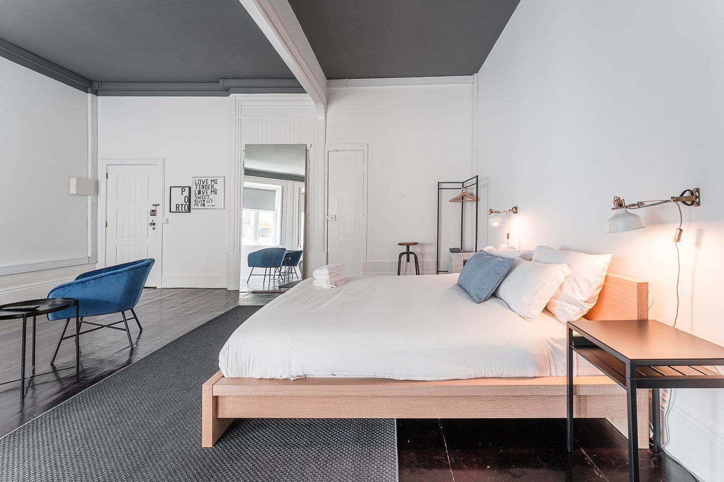 A modern bedroom with a large bed, a desk, a chair, and a bedside table.